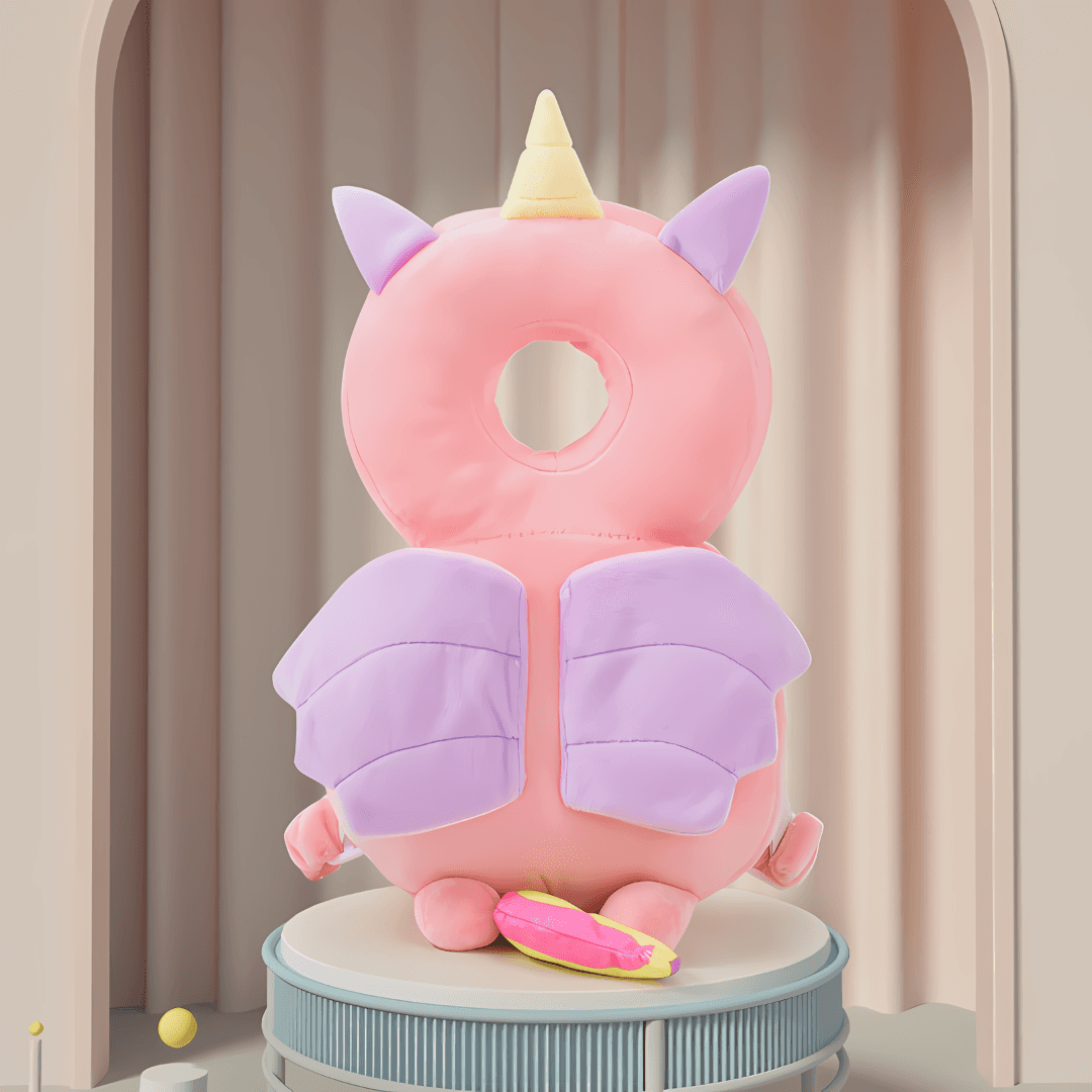 A pastel-colored plush toy designed as a pink and purple winged creature with a circular head and unicorn horn, standing on a round pedestal with a curtain backdrop. The toy's back is facing the viewer, showcasing its wings and tail details.